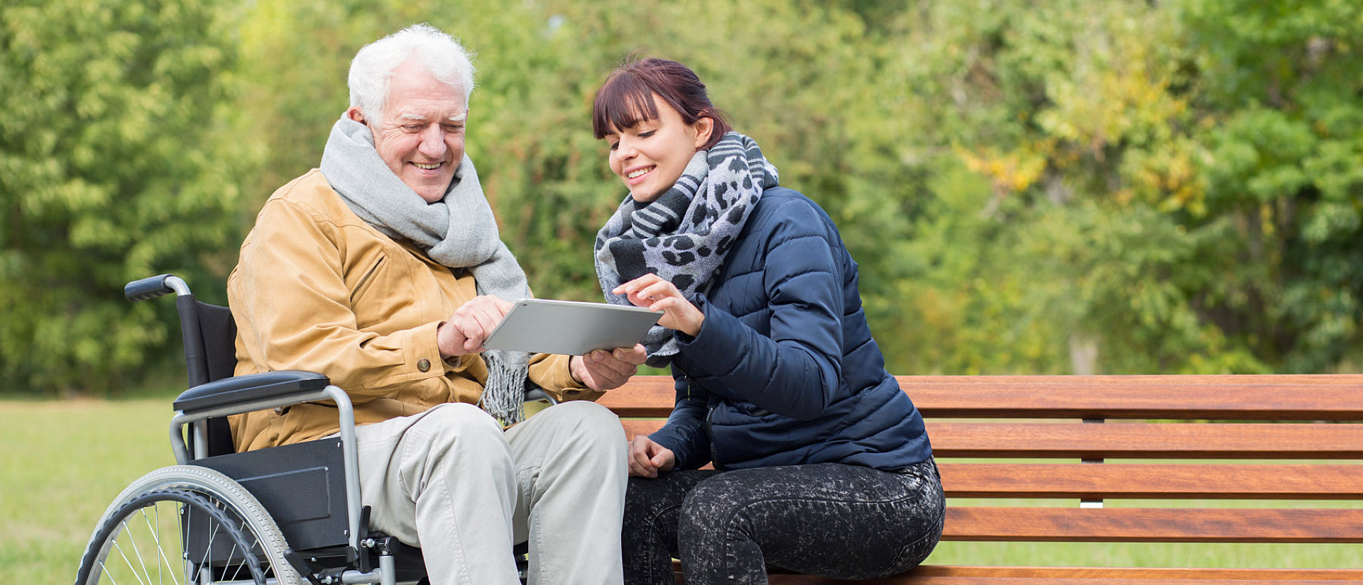 adult woman and senior man on a wheelchair reading on a tablet